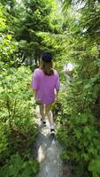 A young woman in a pink shirt and shorts walking through a forest path towards a serene lake, with sunlight filtering through the trees, capturing the essence of outdoor adventure and nature's tranquility video