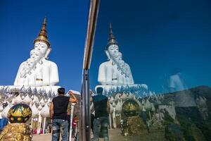 Low back view of a man standing near a transparent glass wall reflecting a large white Buddha statue. photo