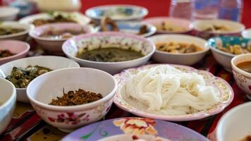 A close-up view of khanom jeen, curry, fried eggs, stir-fries and many other dishes packed in bowls. photo