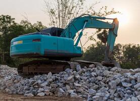 A low-angle view of a green backhoe parked on a pile of granite rubble. photo