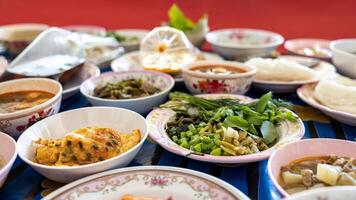 A close-up view of khanom jeen, curry, fried eggs, stir-fries and many other dishes packed in bowls. photo