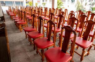 View of wooden chairs and red cushions arranged in rows on the concrete floor. photo