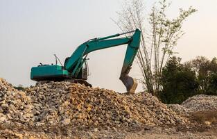 A low-angle view of a green backhoe parked on a pile of granite rubble. photo