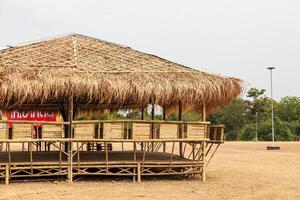 A view of a large bamboo-roofed chair shelter pavilion installed on a mound to shelter. photo