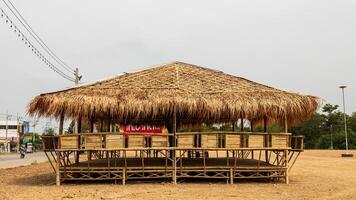 A view of a large bamboo-roofed chair shelter pavilion installed on a mound to shelter. photo