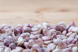 Heap of fresh garlic cloves with peel on wooden table photo