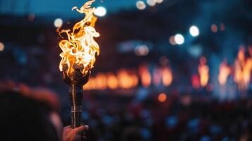 Hand holding a blazing torch aloft with a blurred crowd and evening lights in the background photo