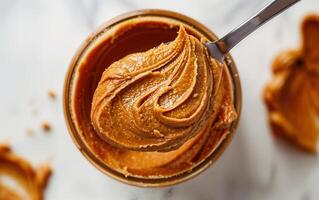 Closeup of smooth peanut butter texture in a glass jar with a spoon photo