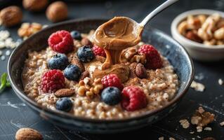 Oatmeal bowl with a spoon of creamy peanut butter, fresh raspberries, blueberries, and nuts on a rustic table photo
