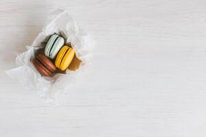 Three French macarons in gift box on a white wooden table. Chocolate, yellow and light blue macarons. photo