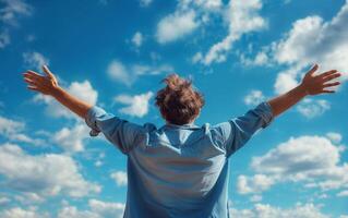Back view of a person with arms wide open against a vibrant blue sky, expressing freedom photo