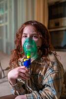 Sick girl making inhalation with nebulizer to reduce coughing, at home, child taking medication while breathing in through face mask. Bronchitis and asthma treatments for children photo