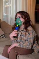 Sick girl making inhalation with nebulizer to reduce coughing, at home, child taking medication while breathing in through face mask. Bronchitis and asthma treatments for children photo