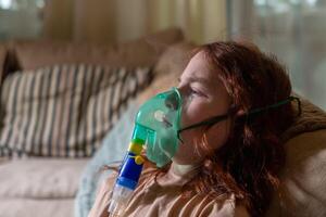 Sick girl making inhalation with nebulizer to reduce coughing, at home, child taking medication while breathing in through face mask. Bronchitis and asthma treatments for children photo