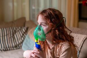 Sick girl making inhalation with nebulizer to reduce coughing, at home, child taking medication while breathing in through face mask. Bronchitis and asthma treatments for children photo