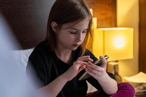 cute little girl on the bed with mobile phone photo