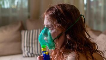 Sick girl making inhalation with nebulizer to reduce coughing, at home, child taking medication while breathing in through face mask. Bronchitis and asthma treatments for children photo