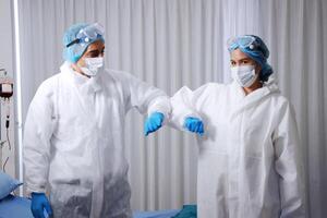 Caucasian and Asian Medical team in Personal Protective Equipment or PPE clothing and Healing for patient infected with the Covid-19 virus is Elbow and arms collide in hospital of Thailand photo