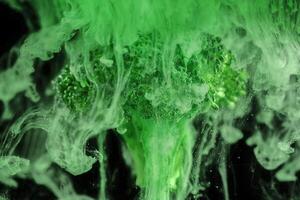 Fresh broccoli with a cloud of green color paint on black background. Artistic nutrition concept. Science of food action photography. photo