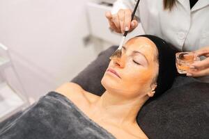 Lady with closed eyes getting facial treatment in beauty salon photo