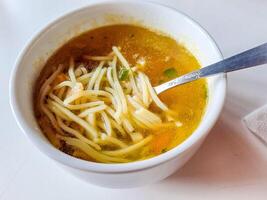 bowl of chicken broth soup with vegetables and vermicelli on white background photo
