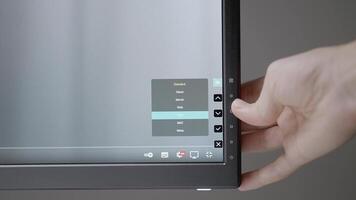 The hand adjusts the monitor to work. ACTION. A black monitor adjusts the hand of a man. A light hand presses the settings buttons on the bottom of the monitor video