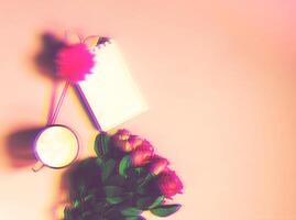 The cup of hot coffee, empty notepad with funny pen and bouquet of fresh roses on soft pink background. Glitch effect image. photo
