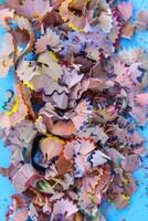 Wooden pencil shavings and colorful crumbs of graphite from sharpener on soft pastel paper background. Top view. Design elements for poster, banner, cards photo