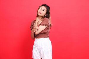 Expression of an indonesia woman with sore shoulders candidly wearing a brown blouse top and shorts on a red background. for health, lifestyle and advertising concepts photo