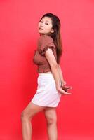 Elegant Asian girl model with her hands behind her back wearing a brown blouse and shorts with a red background. for fashion, lifestyle and clothing concepts photo