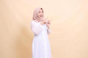 woman asian muslim standing smiling cheerful both hands pointing to the top left. Fashion, pointer, business and promotion concept photo