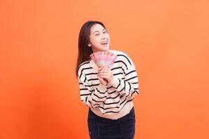 an indonesia woman with a happy expression standing while both hands holding several rupiah notes. for fashion, business and finance concept photo