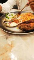 portrait of asian woman's hand taking pickles and sliced onions on a spoon and fork top of plate of nasi kebuli rice kebuli typical arabic food photo