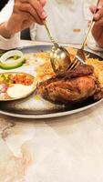 portrait of asian woman's hands slicing chicken with spoon and fork on a plate of nasi kebuli rice kebuli typical arabic food photo