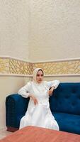 portrait of a beautiful indonesia woman with an elegant expression, both hands resting and sitting on a sofa with an Islamic ornamental calligraphy background, Arabic atmosphere photo