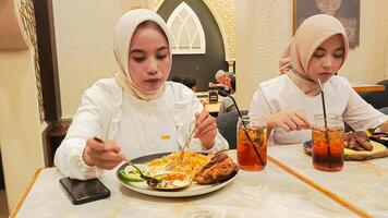 two women are enjoying a meal of kebuli rice and dajaj mashwi oven-roasted chicken and pita bread complete with drinks photo