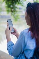 Beautiful Asian woman typing whatsapp message using gadget smart phone in campus park on sunny summer day. female students for education, promotion and lifestyle concepts photo