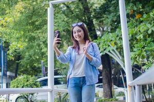 Graceful Asian woman smiling candid call while greeting using smartphone in campus park during sunny day. female students for education, promotion and lifestyle concepts photo