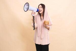 young indonesia woman looks at the camera screaming happily carrying a megaphone loudspeaker and holding a wooden bowl in front of her chest containing delicious dimsum photo