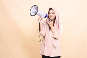indonesia woman looks at the camera with her right hand holding the audio and holding a megaphone loudspeaker smiling and giving an announcement. young beautiful for business, technology, fashion photo