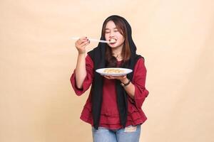beautiful mature Asian girl wearing a red dress wearing a hijab with a delicious smile, closing her eyes, biting into dimsum using chopsticks and carrying a plate containing dimsum Chinese food photo