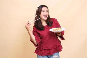 Beautiful Asian woman in red, smiling cheerfully, carrying a plate containing dim sum Chinese food and sauce with chopsticks to the side. used for food, health and lifestyle content photo