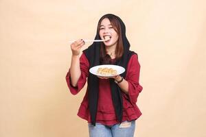beautiful mature Asian woman wearing a red hijab, smiling, biting dimsum, using chopsticks up and carrying a plate containing dimsum Chinese food looking at the camera. used for culinary content photo