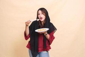 A beautiful mature Asian woman in a red dress wearing a hijab is devouring by lifting dimsum with chopsticks and carrying a plate containing dimsum Chinese food. used for food and culinary content photo