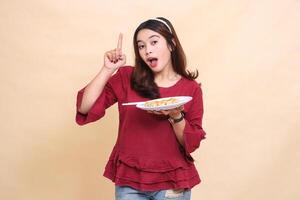 Beautiful young Asian woman in red shirt carrying a plate containing dimsum Chinese food and chopsticks while pointing upwards. used for food, health and lifestyle content photo