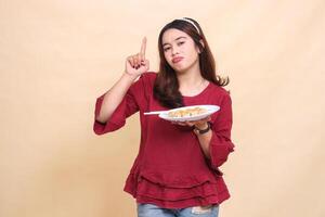 Beautiful young indonesia woman in red pouting carrying a plate of dimsum Chinese food and chopsticks while pointing upwards. used for food, health and lifestyle content photo