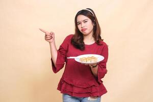 Beautiful young Asian girl in red shirt is disappointed carrying a plate containing dimsum Chinese food and chopsticks while pointing to the right. used for food, health and lifestyle content photo
