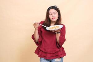 beautiful young indonesia woman in red pouting lifting a plate containing dimsum chinese food and sauce with chopsticks down picking it up. used for food, health and lifestyle content photo