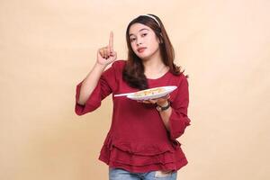 Beautiful young indonesia girl in red dress with flat face carrying a plate containing dimsum Chinese food and chopsticks while pointing upwards. used for food, health and lifestyle content photo