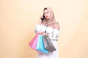 a young Asian Muslim girl in a hijab frowns at someone's phone looking ahead and carrying a paperbag shopping bag. for advertising, technology, Eid and Ramadan photo